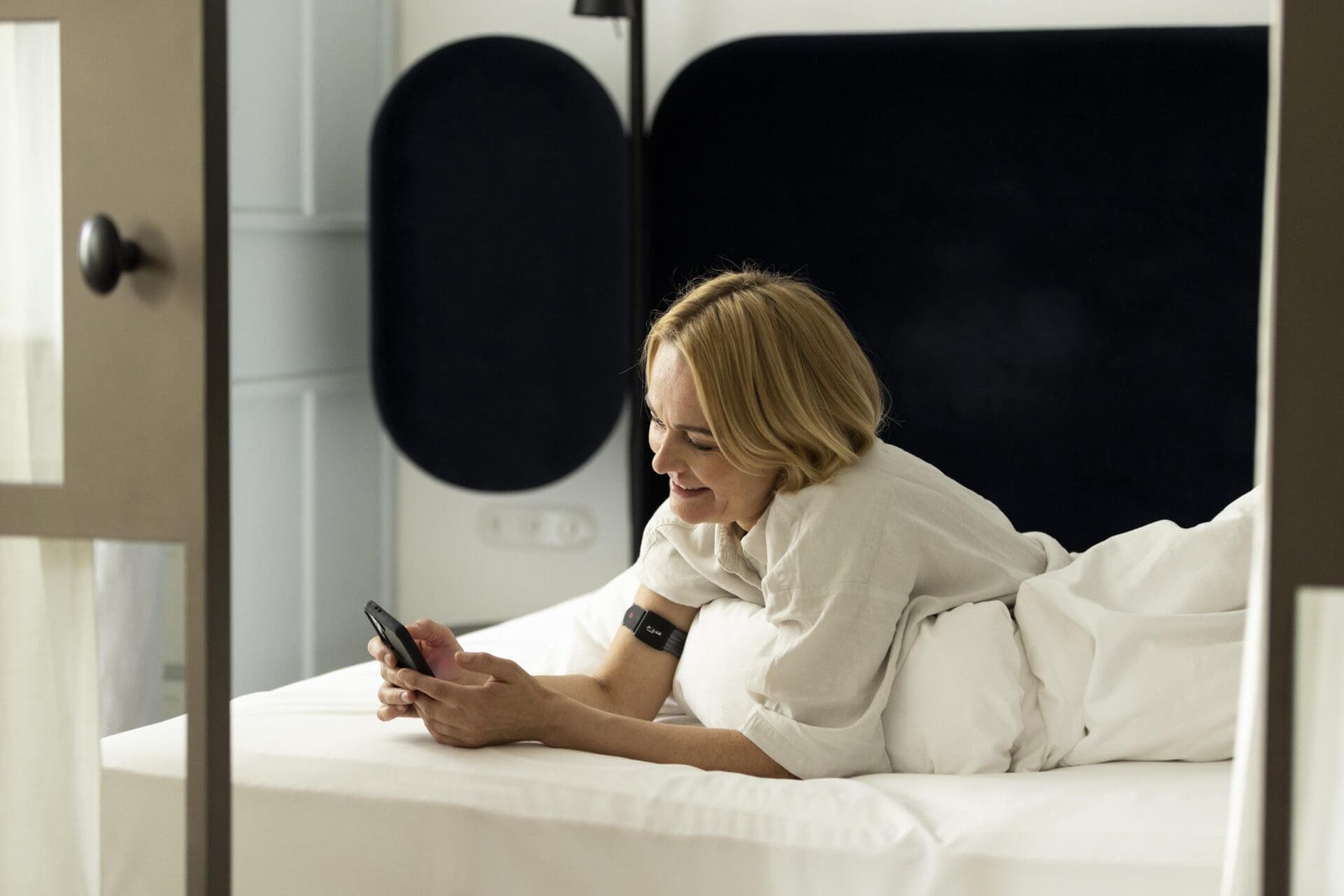 Frau liegt im Bett, nachdem sie ihre Schlaf gemessen hat und sieht sich die Ergebnisse an.