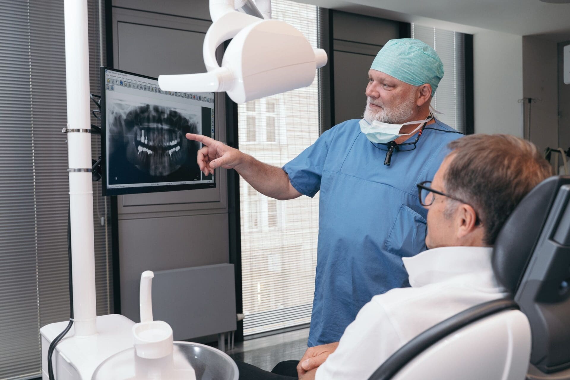 Ein Kieferchirurg zeigt im Gespräch mit einem Patienten auf ein Röntgenbild.